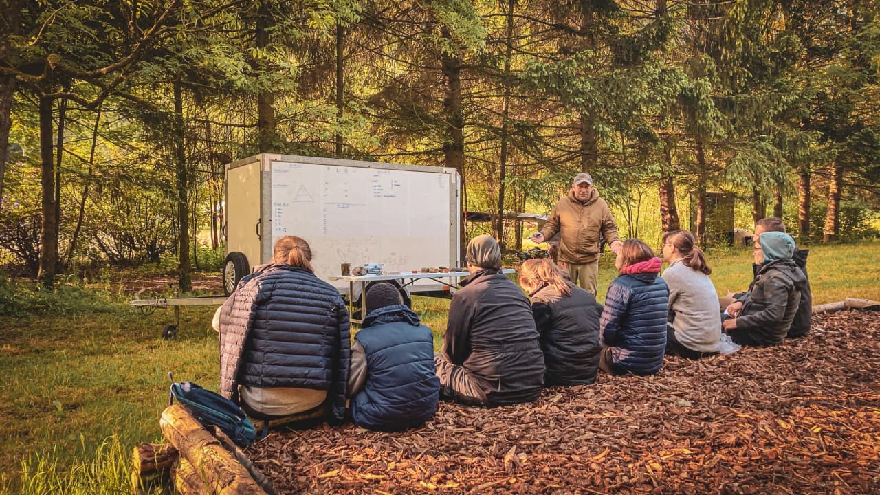 Groupe de participants écoutant un instructeur lors d'un stage de survie en forêt en Ardenne.