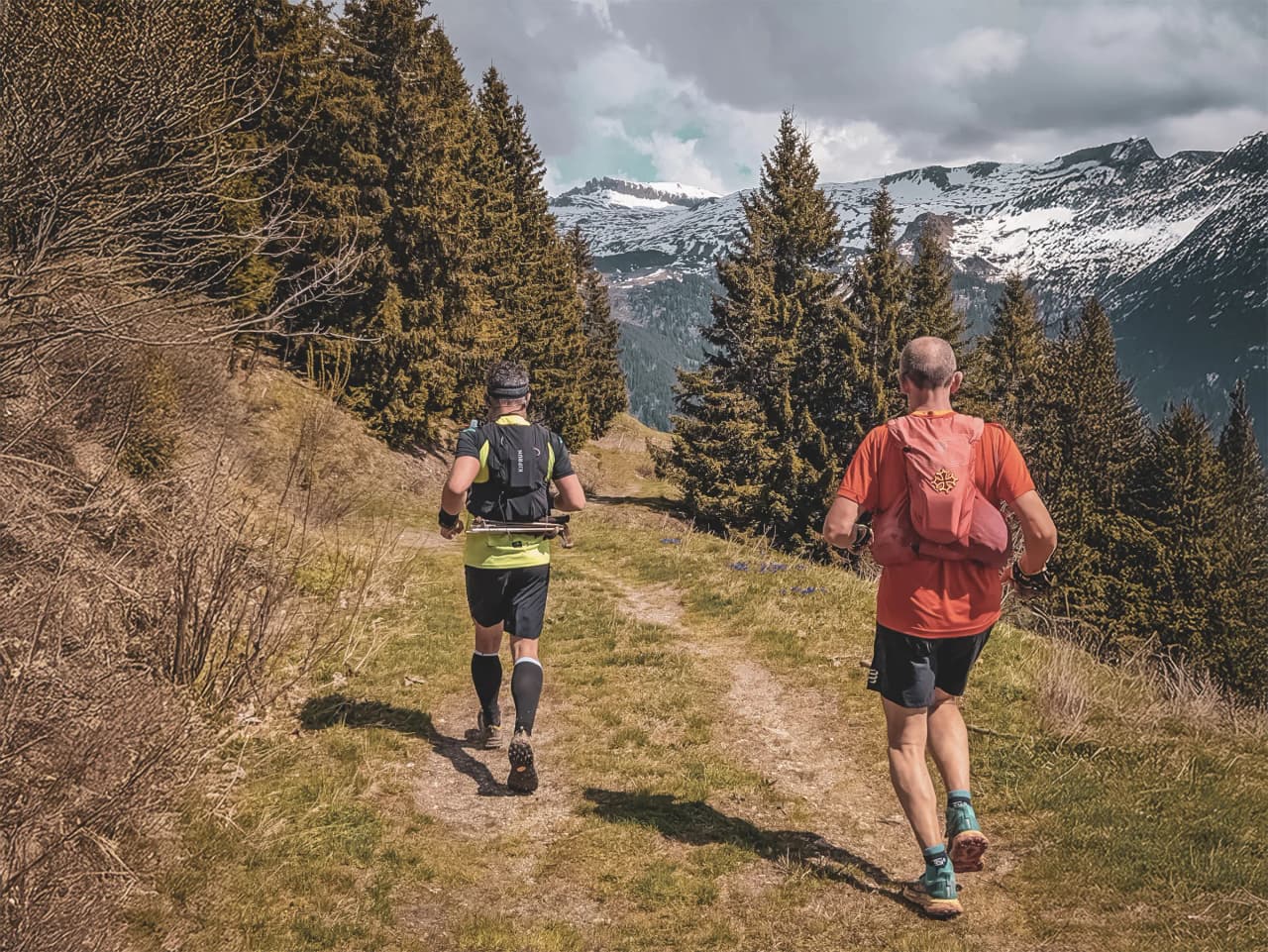 Deux coureurs en trail sur un chemin ensoleillé, entourés de majestueux paysages alpins.