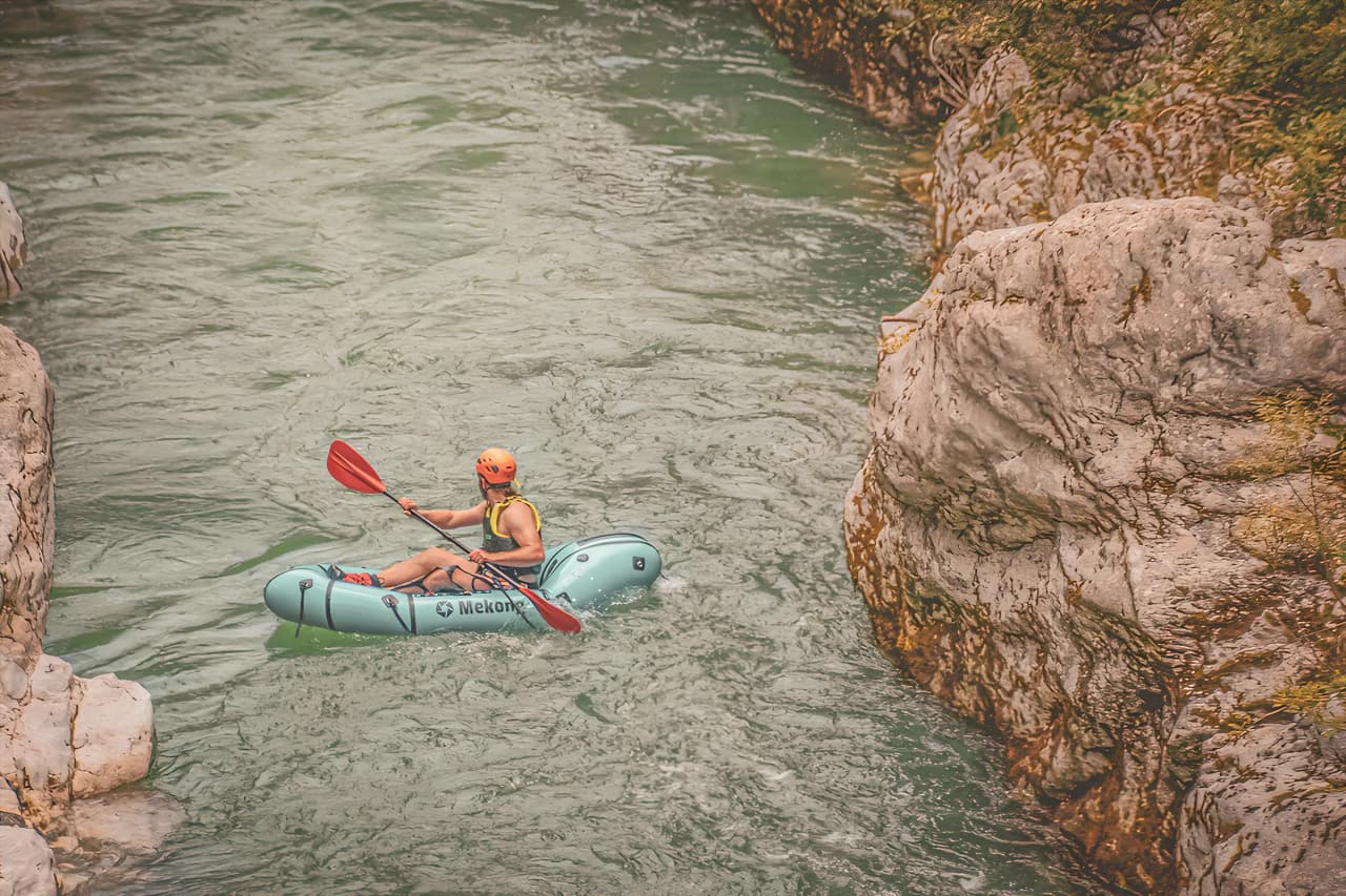 A packraft adventurer navigates an Alpine river surrounded by majestic cliffs.