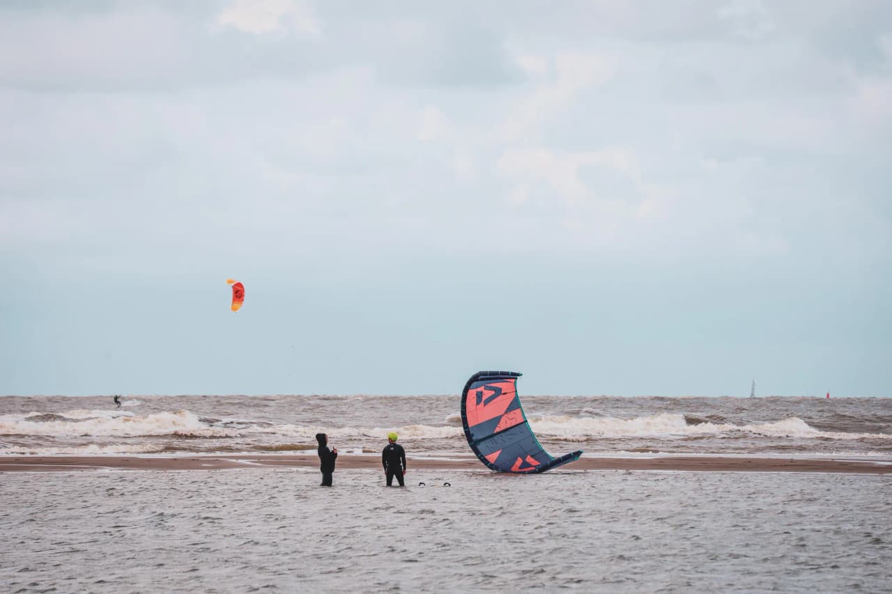 Two kitesurfers at the seaside, enjoying the waves and a cloudy sky in Zeeland.
