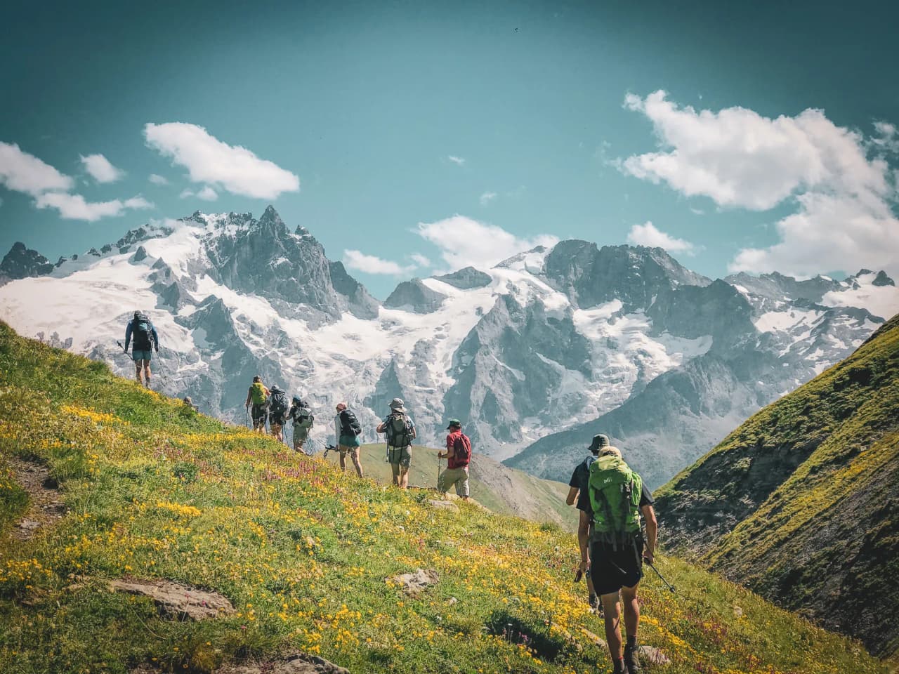 Randonneurs sur un sentier fleuri, entourés de majestueuses montagnes aux neiges éternelles.