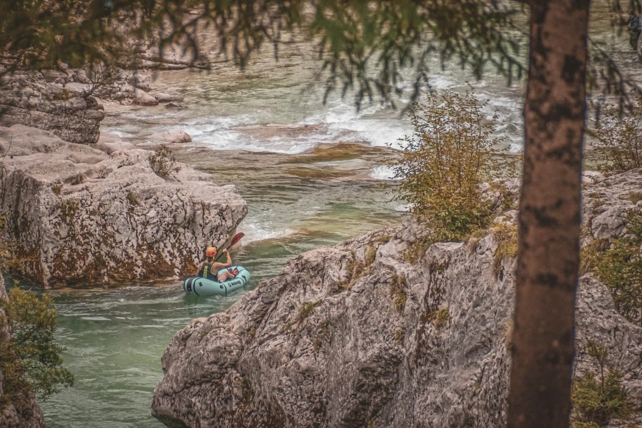 Packraft hiker navigating between rocks on a crystal-clear river in Slovenia.