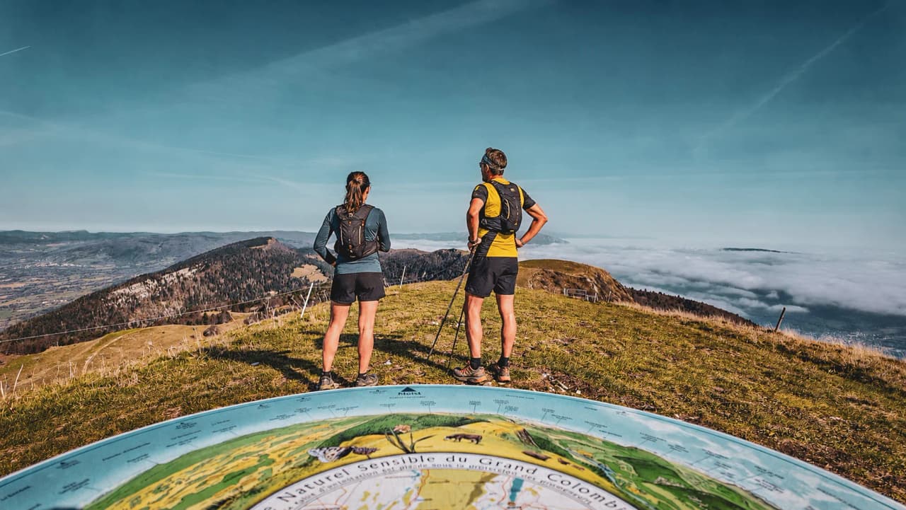 Two hikers admire the panorama of the Jura massif, facing Lac du Bourget.