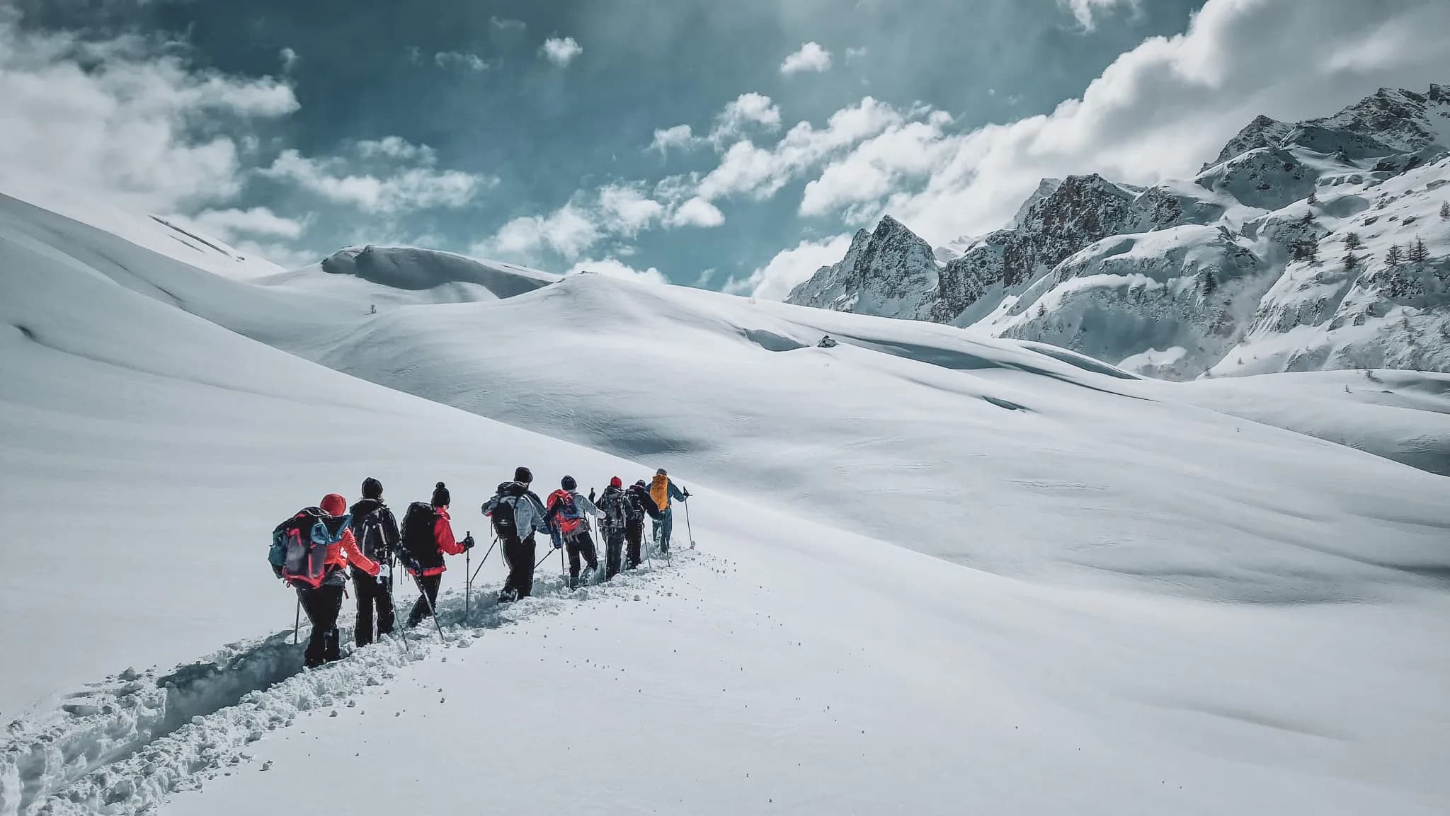 Groep wandelaars op sneeuwschoenen in een besneeuwd alpenlandschap, met bergen op de achtergrond.