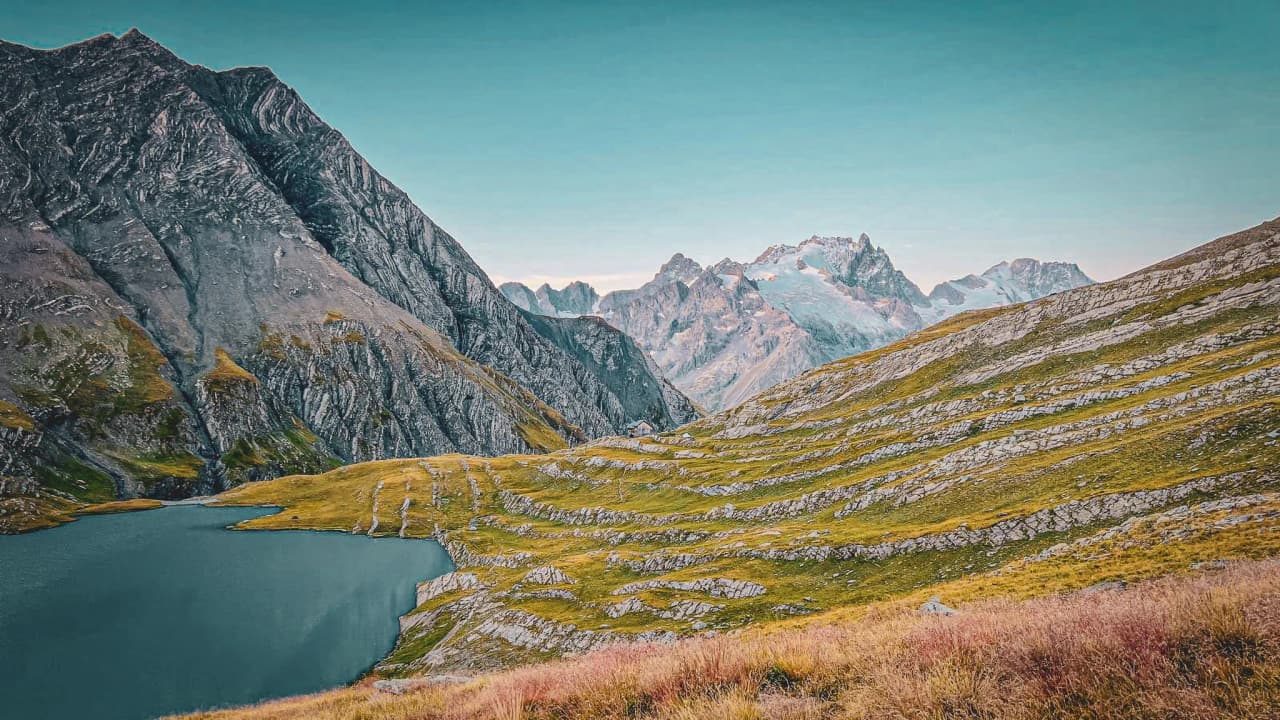 Montagnes majestueuses, lac turquoise et prairies verdoyantes sous un ciel clair. Évasion alpine.