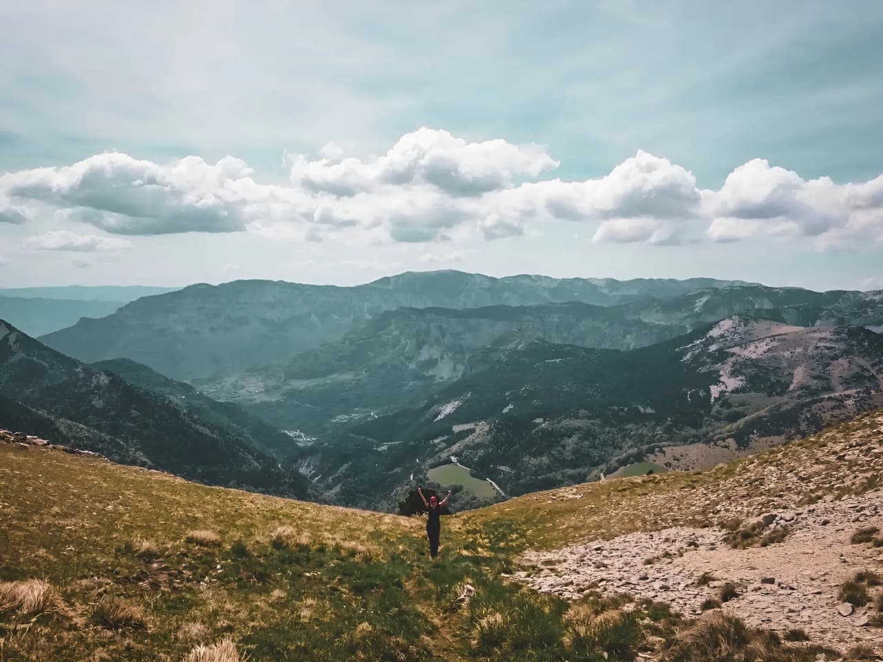 A happy hiker stretches out his arms in front of a majestic panorama of the Vercors mountains.
