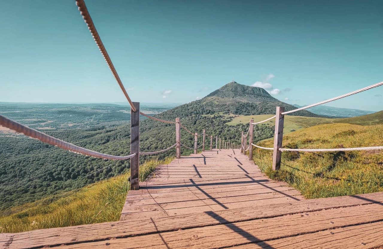 A wooden path winding through the volcanic landscapes of the Auvergne, under a blue sky.