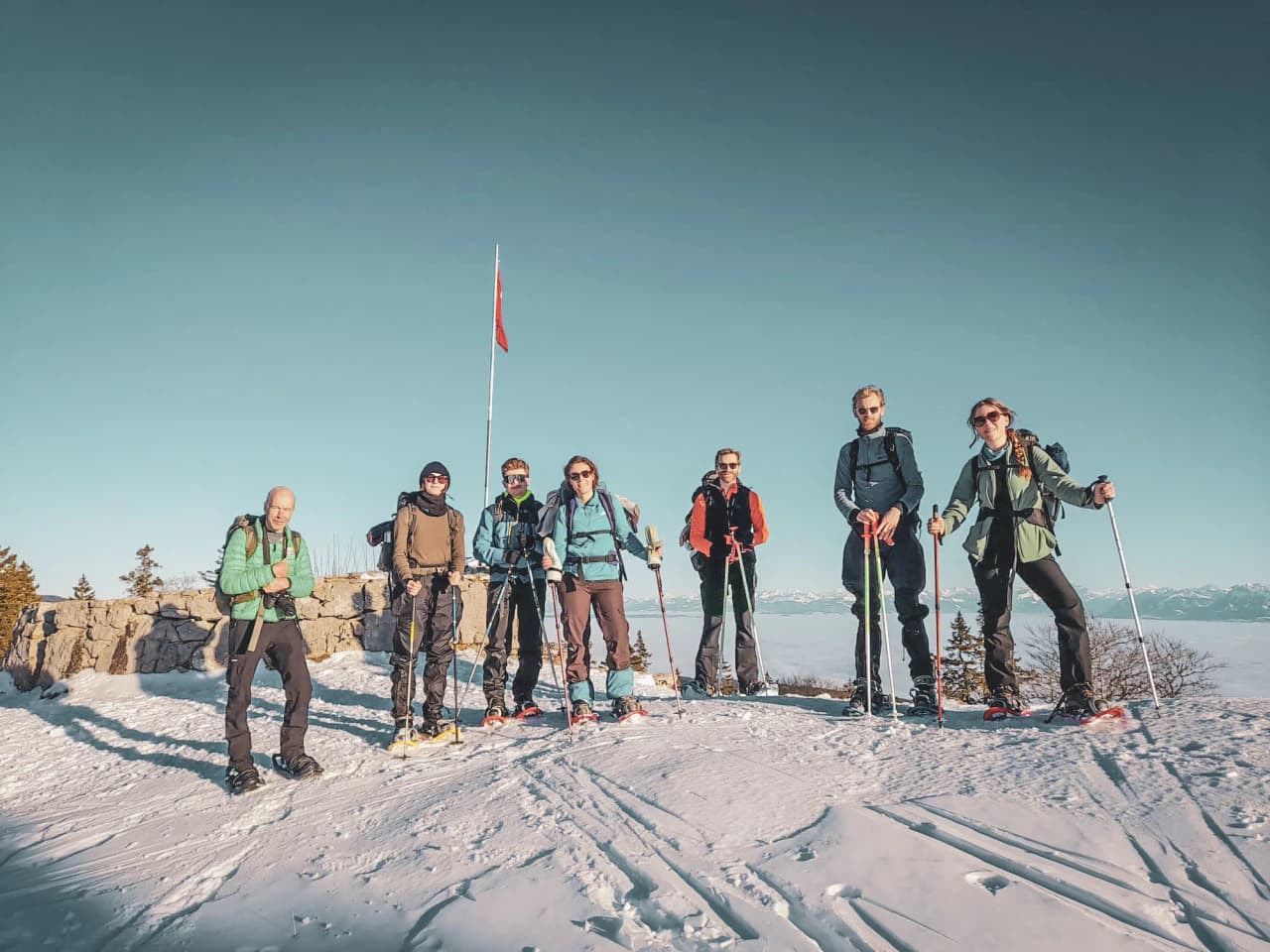 Groupe de randonneurs en raquettes, sur fond de neige, admirant un panorama alpin.