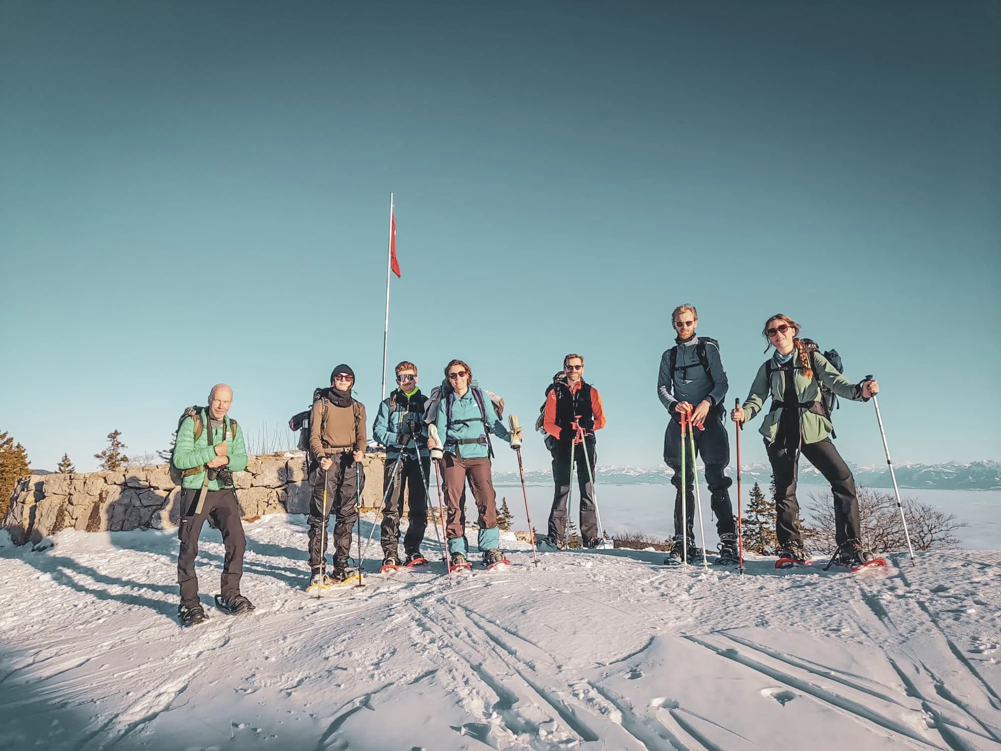 Groupe de randonneurs en raquettes, sur fond de neige, admirant un panorama alpin.