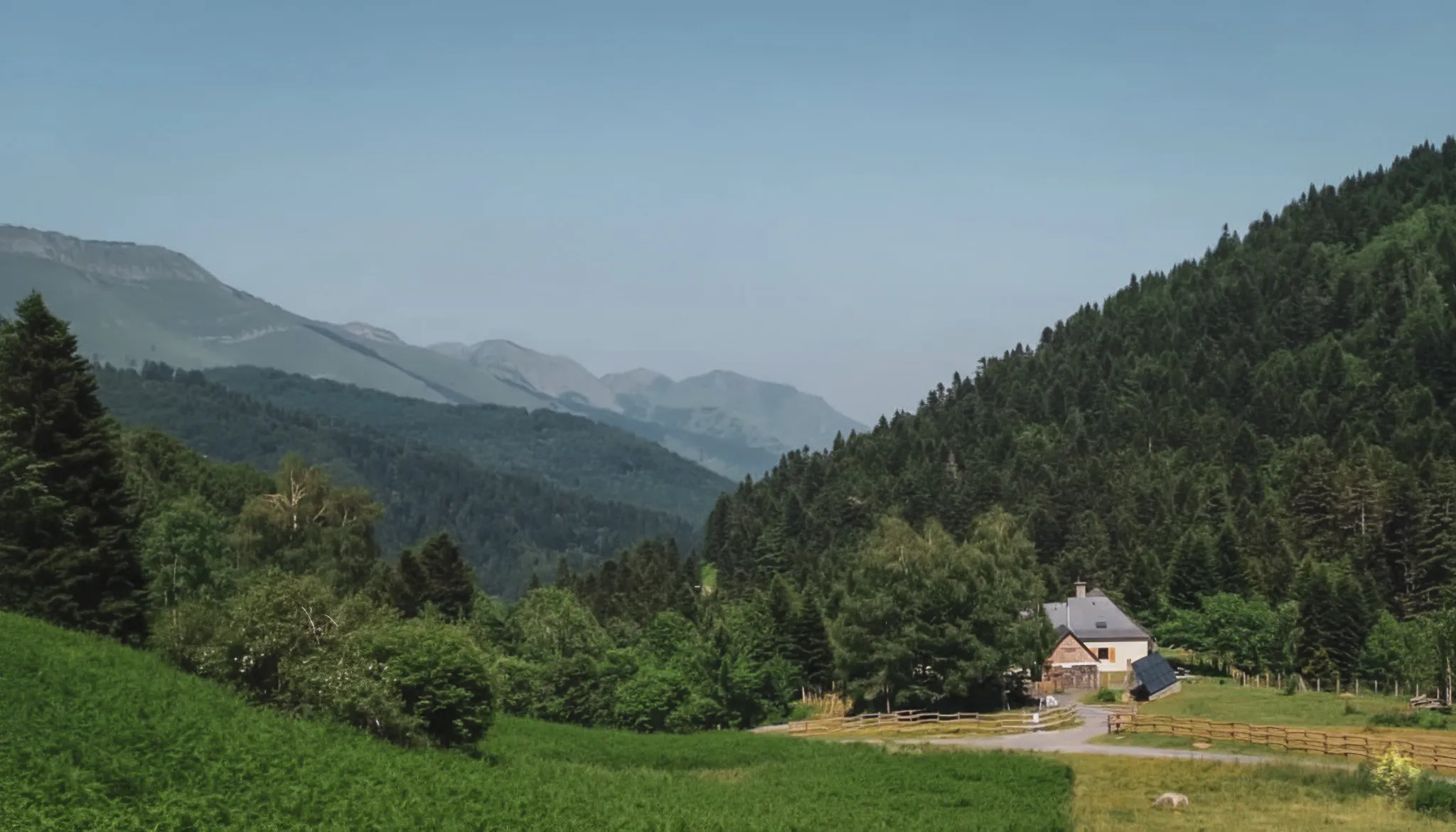 Vaste panorama des Pyrénées, alliant nature verdoyante et paisible maison de montagne.