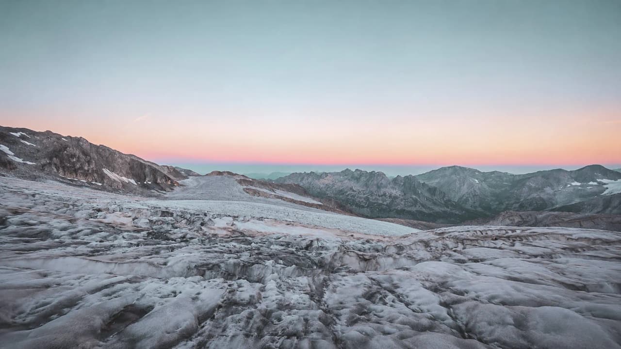 Un vaste glacier aux teintes pastel, bordé de majestueuses montagnes, invite à l'aventure alpine.