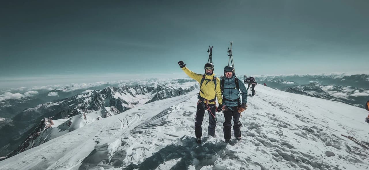 Deux skieurs souriants sur le sommet du Mont Blanc, entourés de paysages alpins à couper le souffle.