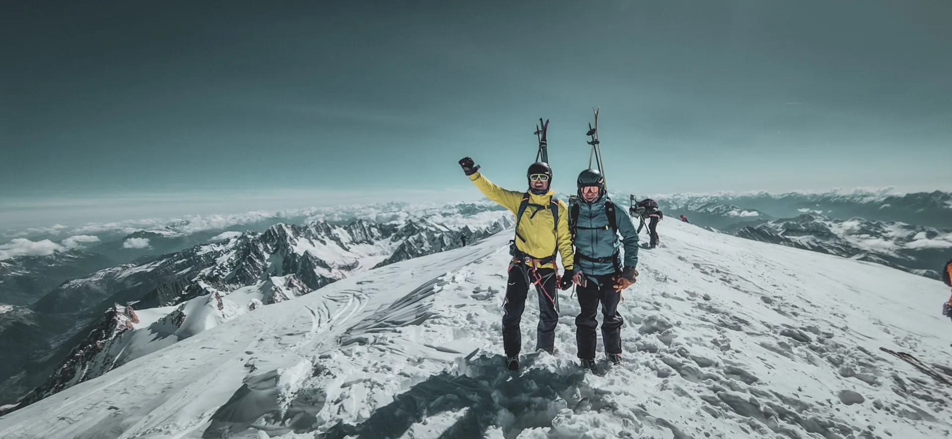 Twee lachende skiërs op de top van de Mont Blanc, omringd door adembenemende Alpenlandschappen.