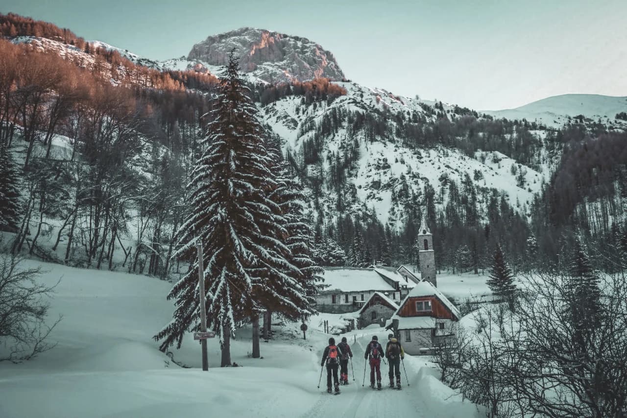 Un groupe de randonneurs en raquettes marchant dans un paysage enneigé, entouré de montagnes majestueuses.