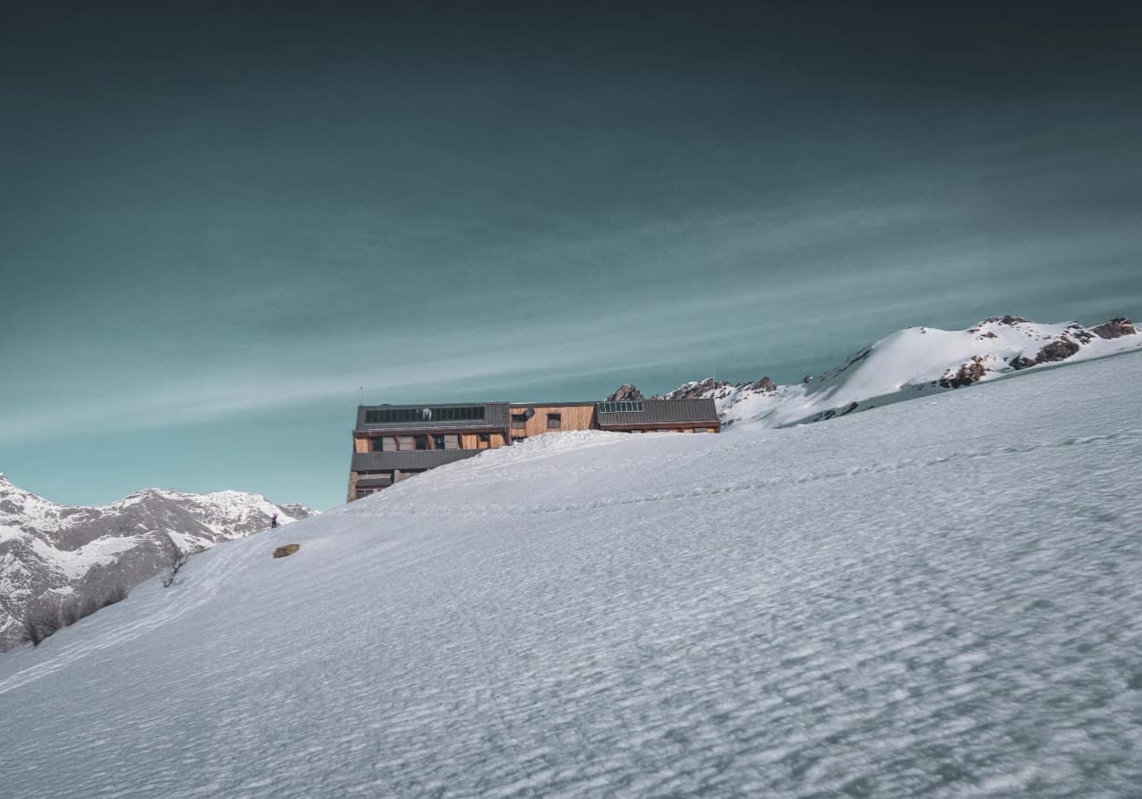Refuge montagnard isolé, enneigé, sous un ciel bleu clair, offrant une vue sur les sommets alpins.