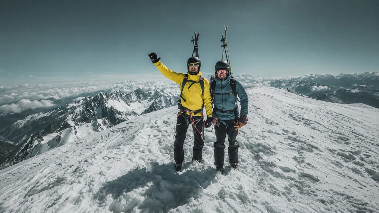 Twee lachende skiërs op de top van de Mont Blanc, omringd door adembenemende Alpenlandschappen.
