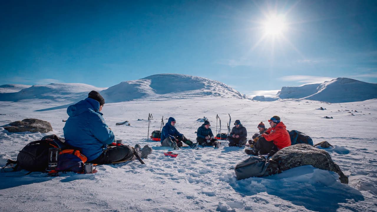 Een groep skiërs op de Kungsleden, die onder een stralende zon genieten van een maaltijd midden in de natuur.