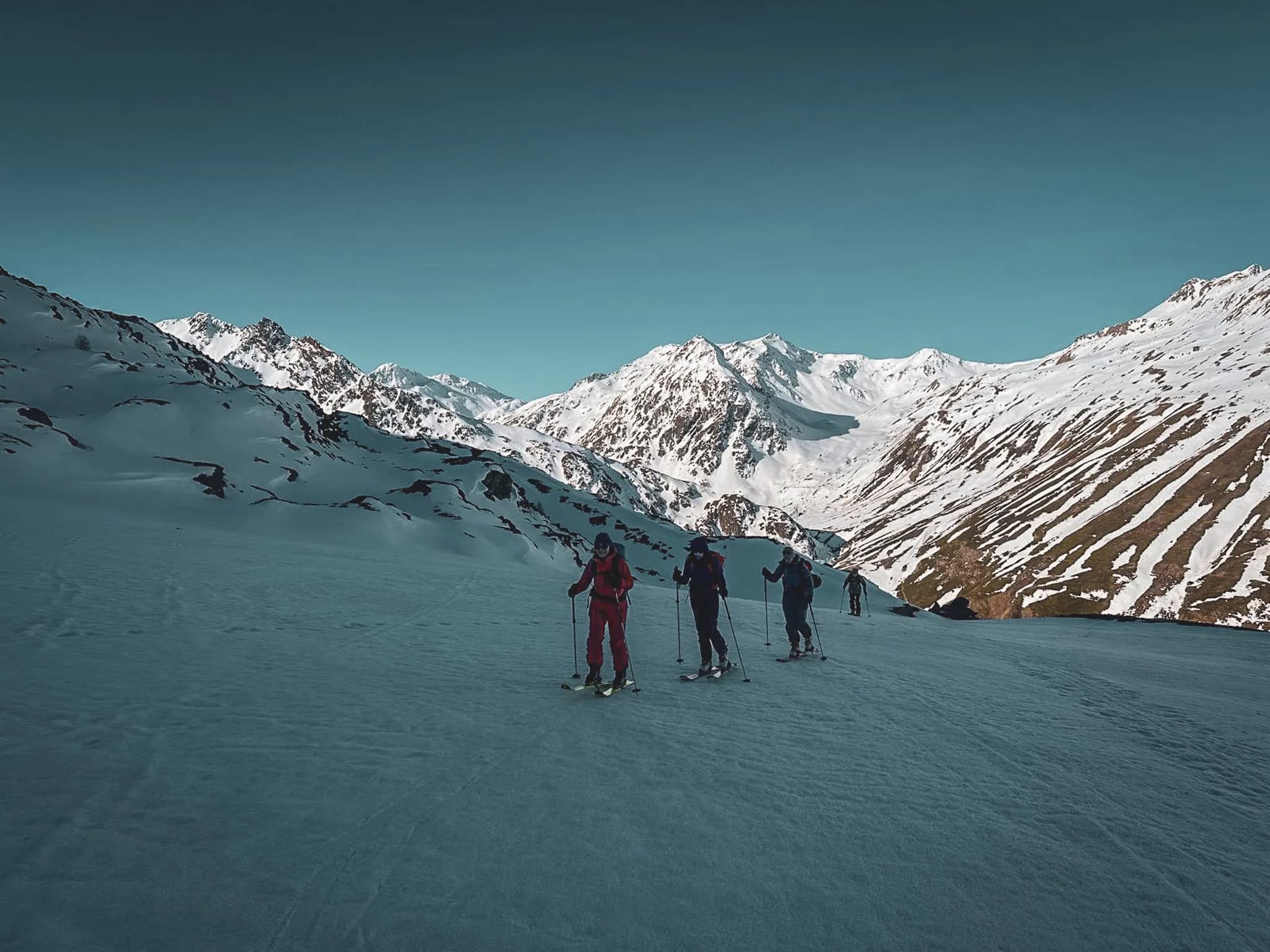 A group of skiers on an alpine tour, facing the snow-capped peaks of the Great Saint Bernard Pass.