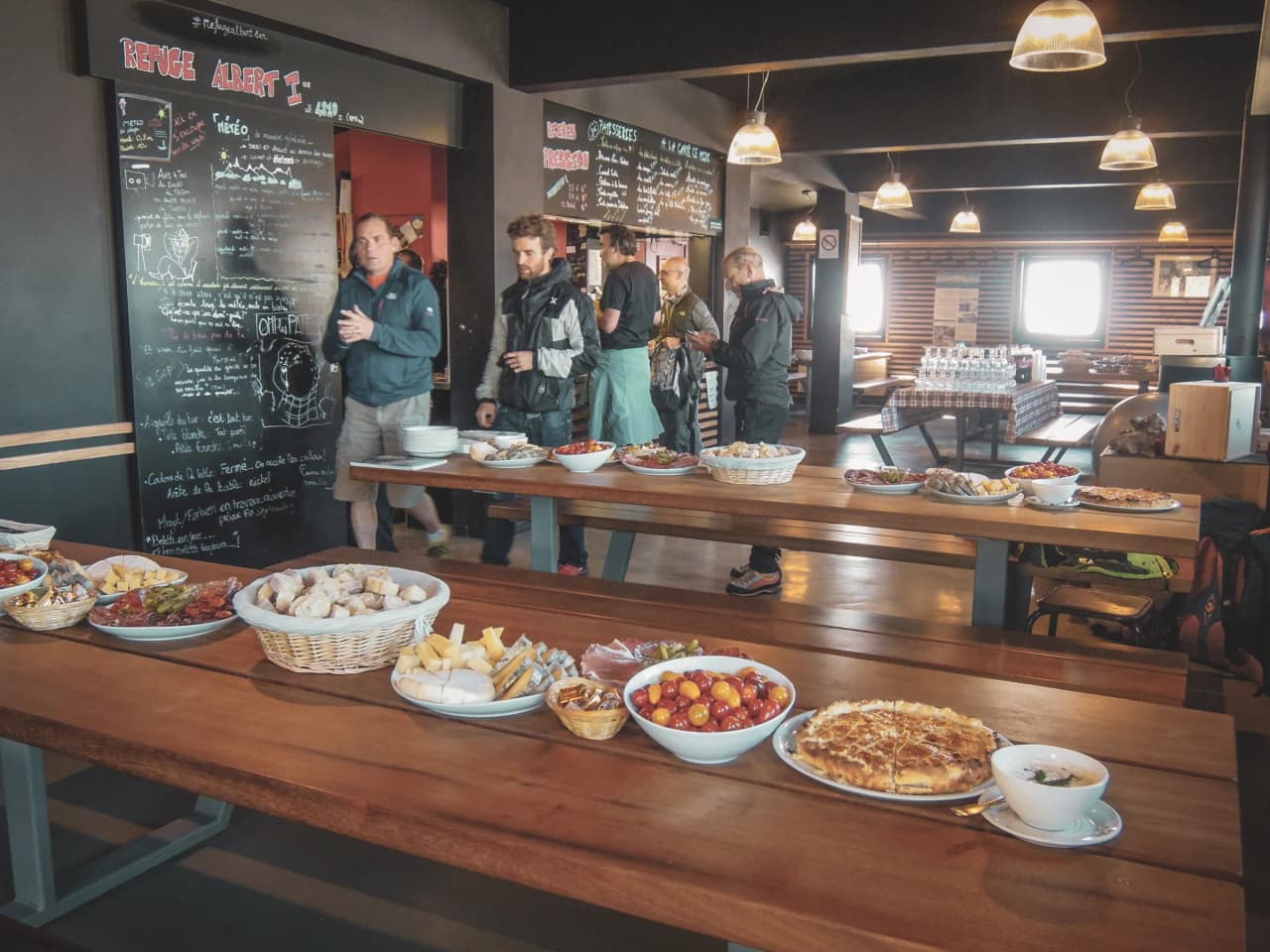 Une salle chaleureuse avec des tables en bois, des plats savoureux et des alpinistes en visite.
