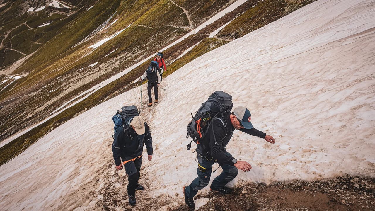 Three hikers climb a glacier, surrounded by breathtaking Alpine panoramas.