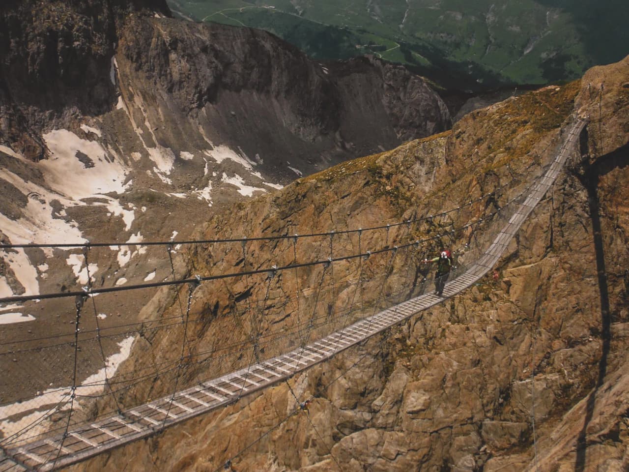 Een wandelaar steekt een hangbrug over majestueuze Alpenlandschappen over.