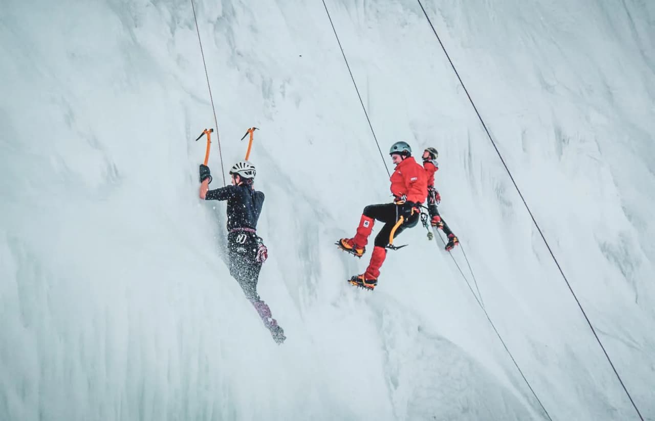 Trois grimpeurs s'attaquent à une cascade de glace, enveloppés par le paysage alpin.