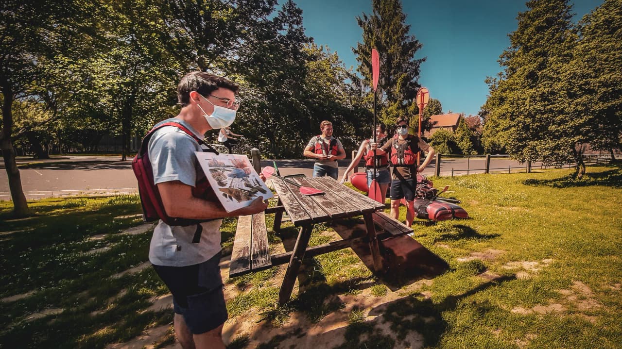 Een groep staat op het punt het Belgische platteland te verkennen in een packraft, omringd door weelderige groene bomen.