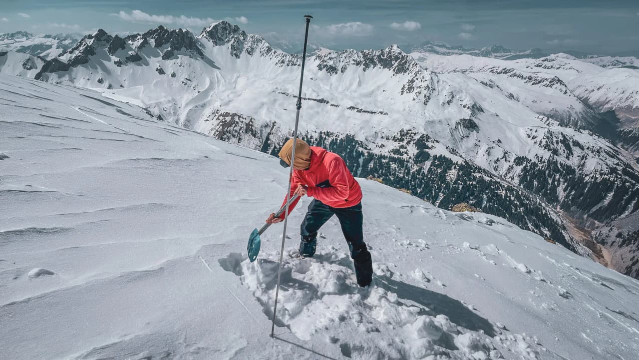 People digging in the snow, majestic mountains in the background, incredible scenery.