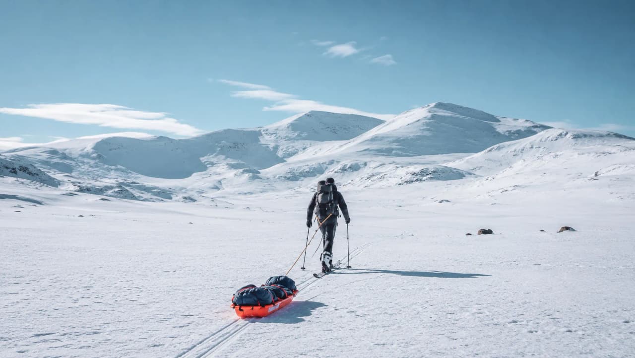Een avonturier trekt een pulka over de sneeuw, omringd door majestueuze bergen in Zweeds Lapland.