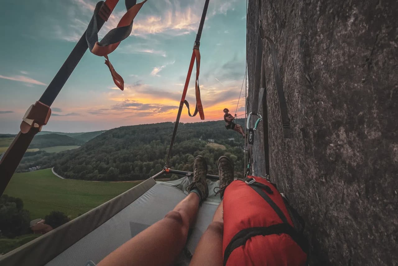 Escalade au coucher de soleil, portaledge suspendu au-dessus de la vallée verdoyante.