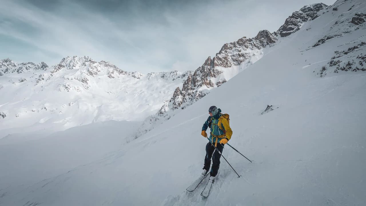 A lone skier explores a majestic snowscape with mountains in the background.
