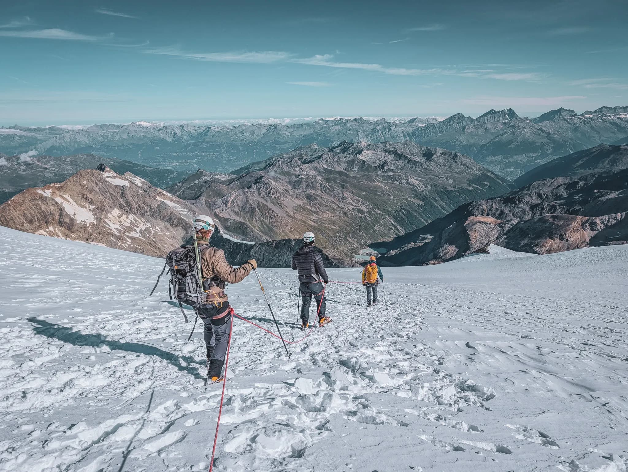 Mountaineers crossing a sun-drenched glacier, with majestic peaks in the background.