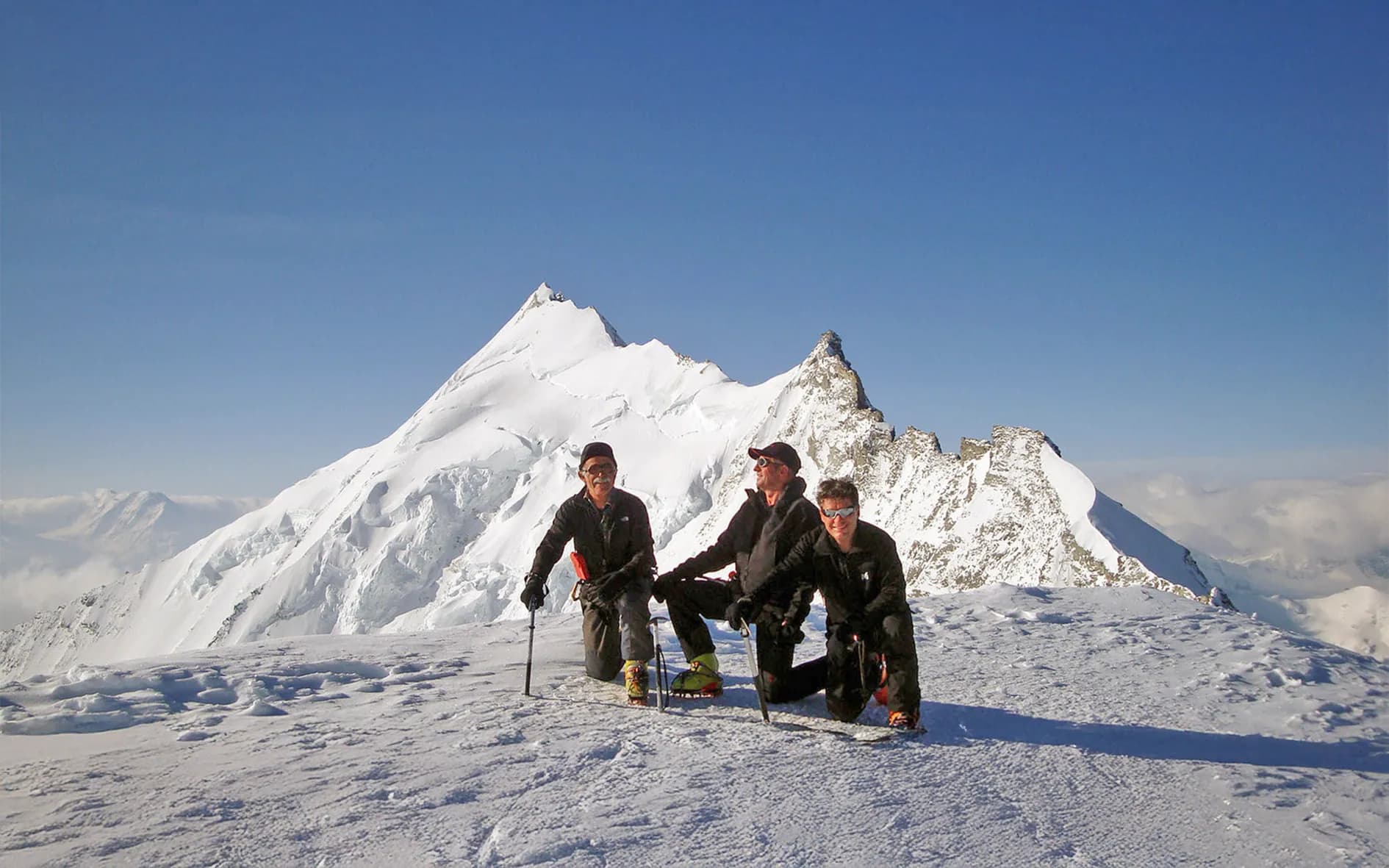 Three climbers in conquest mode on a snow-covered Alpine peak, surrounded by majestic panoramas.