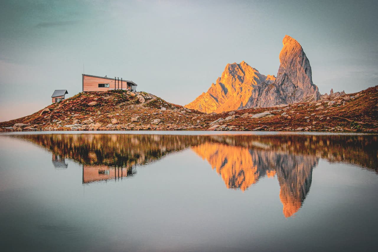 Refuge montagnard au bord d'un lac, reflet des sommets dorés du Beaufortain au lever du soleil.