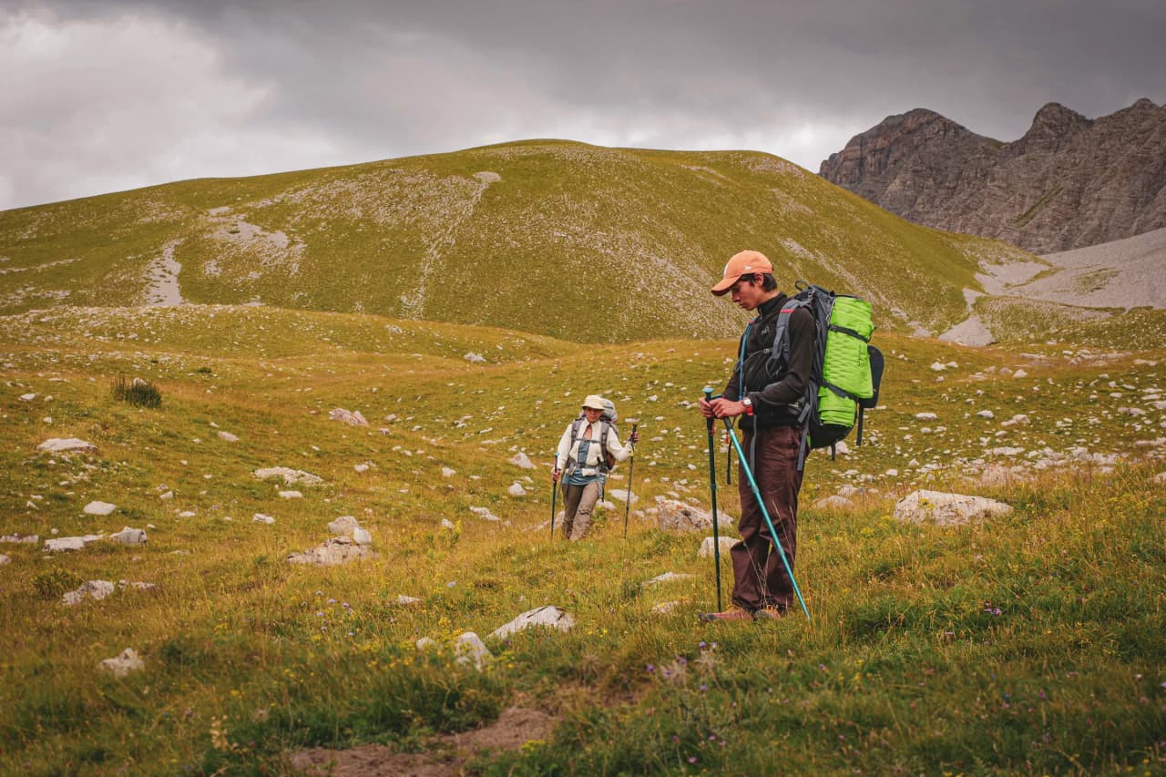 Deux randonneurs explorent des plateaux verdoyants, entourés de montagnes majestueuses.