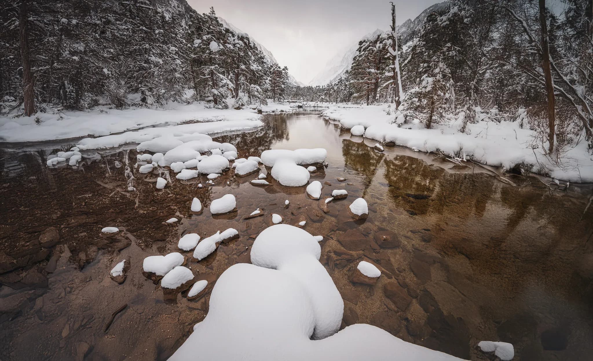 An enchanting landscape: a stream meandering through snow-covered rocks under a cloudy sky.