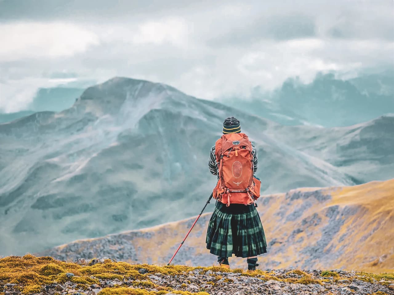 Een wandelaar bewondert de majestueuze landschappen van de Highlands, draagt een kilt en een rugzak.