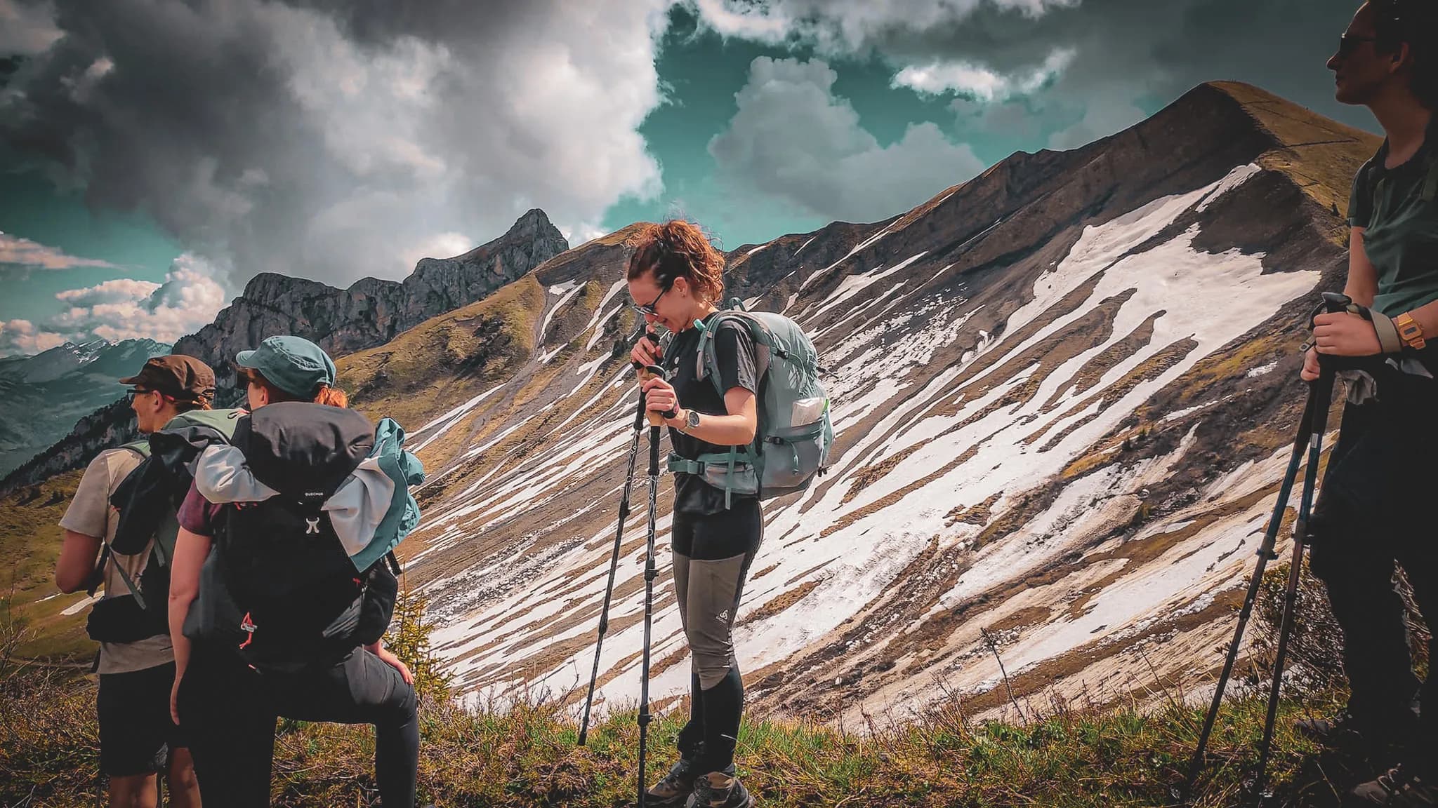 Un groupe de randonneurs se trouve sur un majestueux sentier de montagne, entouré de paysages alpins. L'un des randonneurs, une femme avec un sac à dos, examine une carte ou son équipement, tandis que