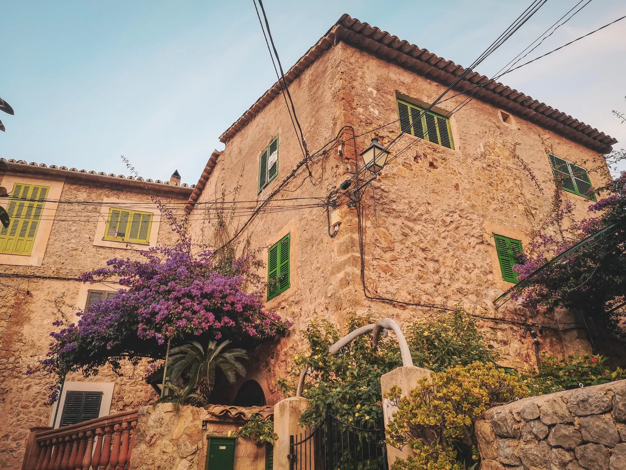 Stone house in Majorca, adorned with purple bougainvillea and green shutters. A charming, peaceful spot.