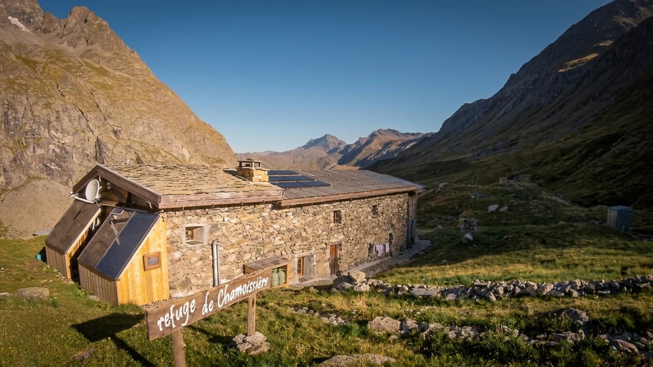 Refuge en pierre entouré de montagnes, avec un ciel bleu clair, invitant à l'aventure alpine.
