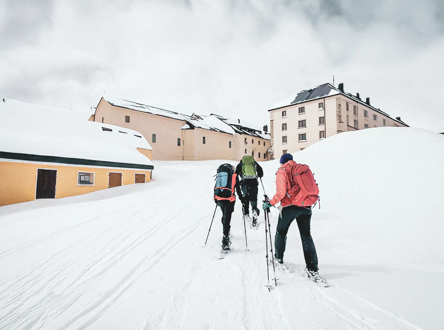 Drie wandelaars op sneeuwschoenen banen zich een weg door de sneeuw in de richting van het Sint-Bernardus Gasthuis.