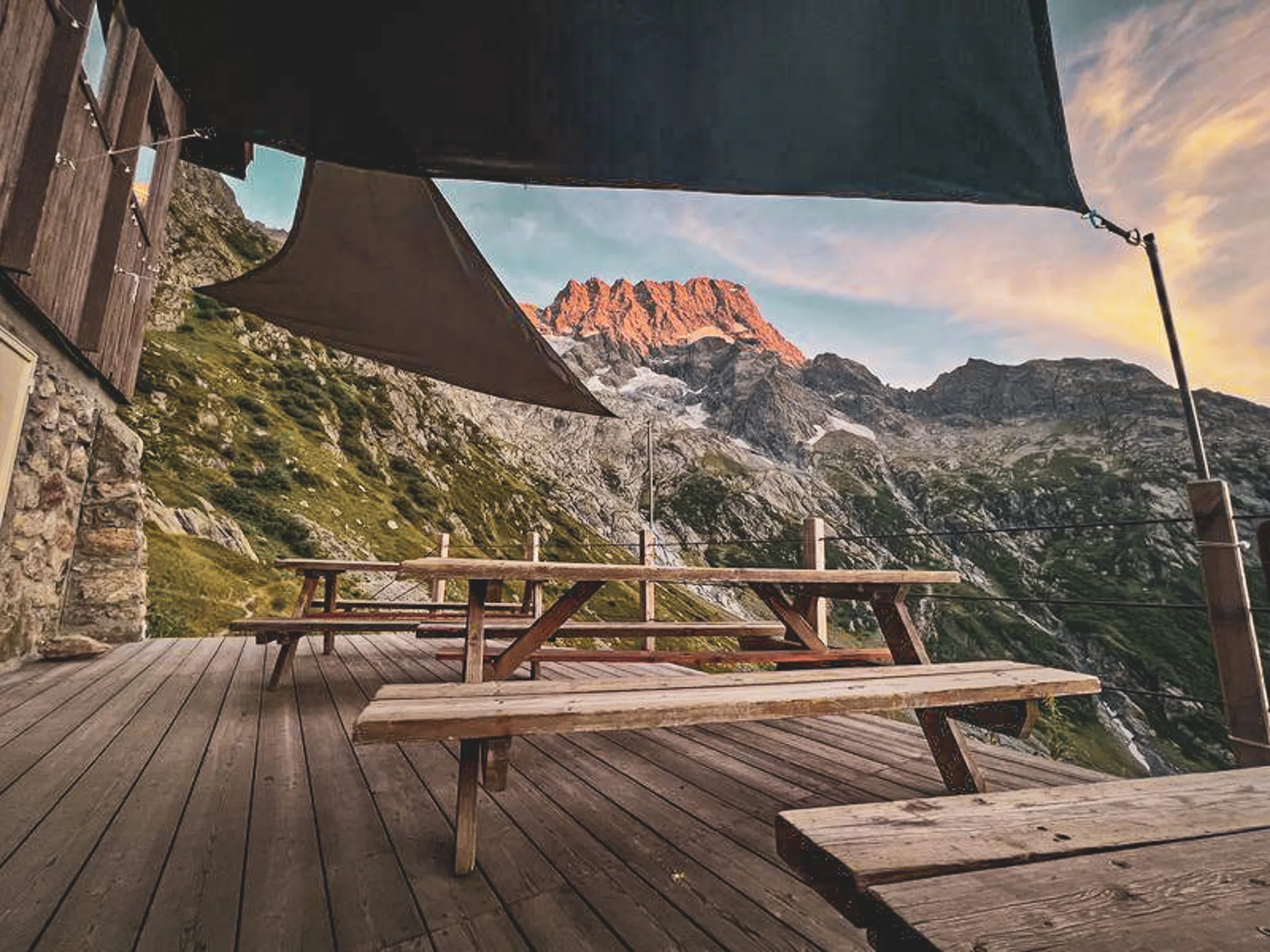 Houten terras met tafels, uitzicht op majestueuze bergen bij zonsondergang. Ontsnapping in de Alpen.