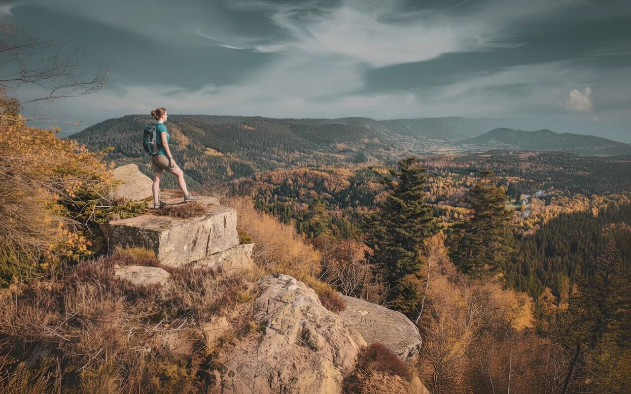 Un randonneur contemplant les paysages colorés des Vosges depuis un rocher. Aventure en pleine nature.