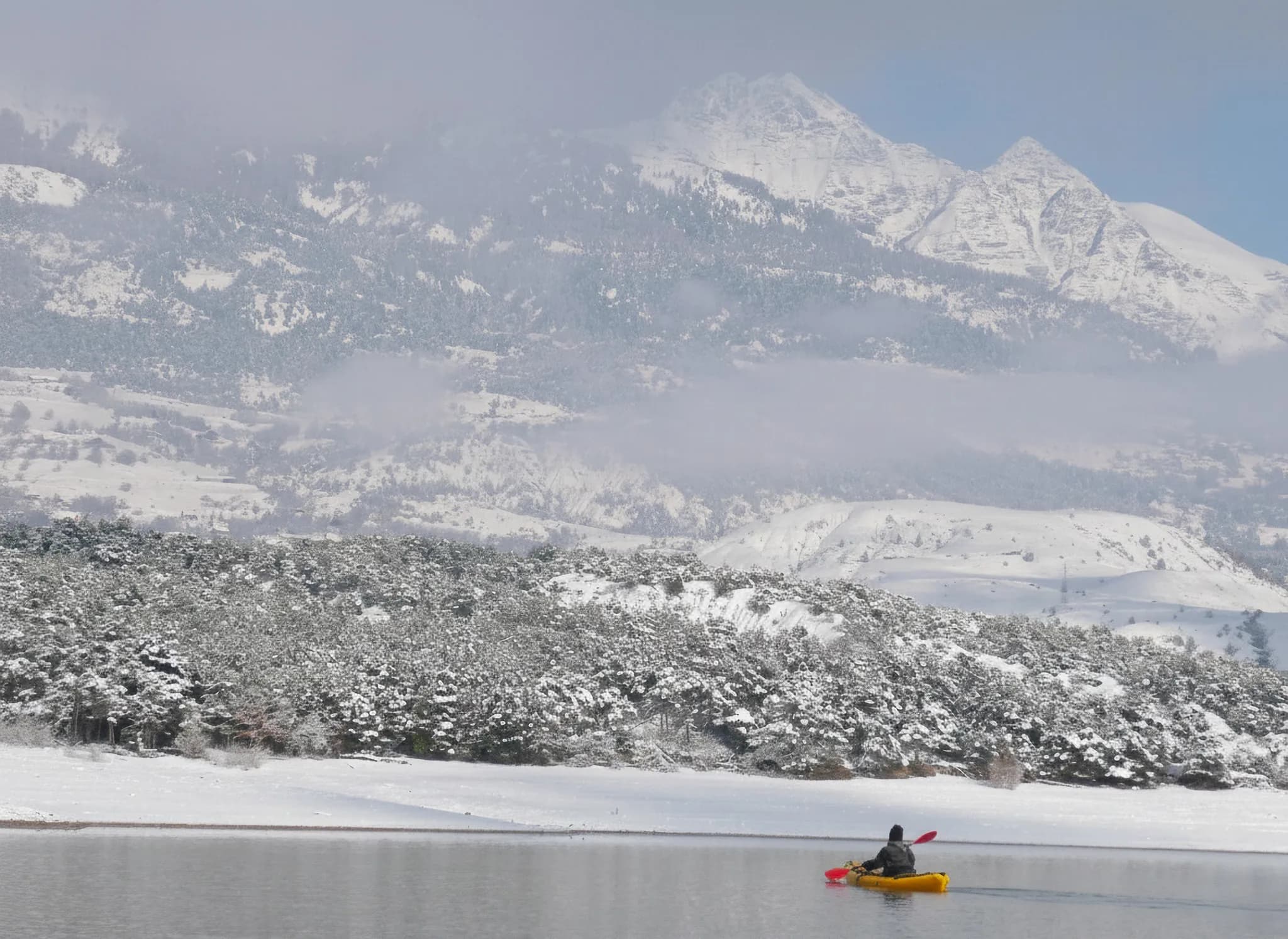 Un aventurier en packraft sur le lac gelé de Serre-Ponçon, entouré de montagnes enneigées.