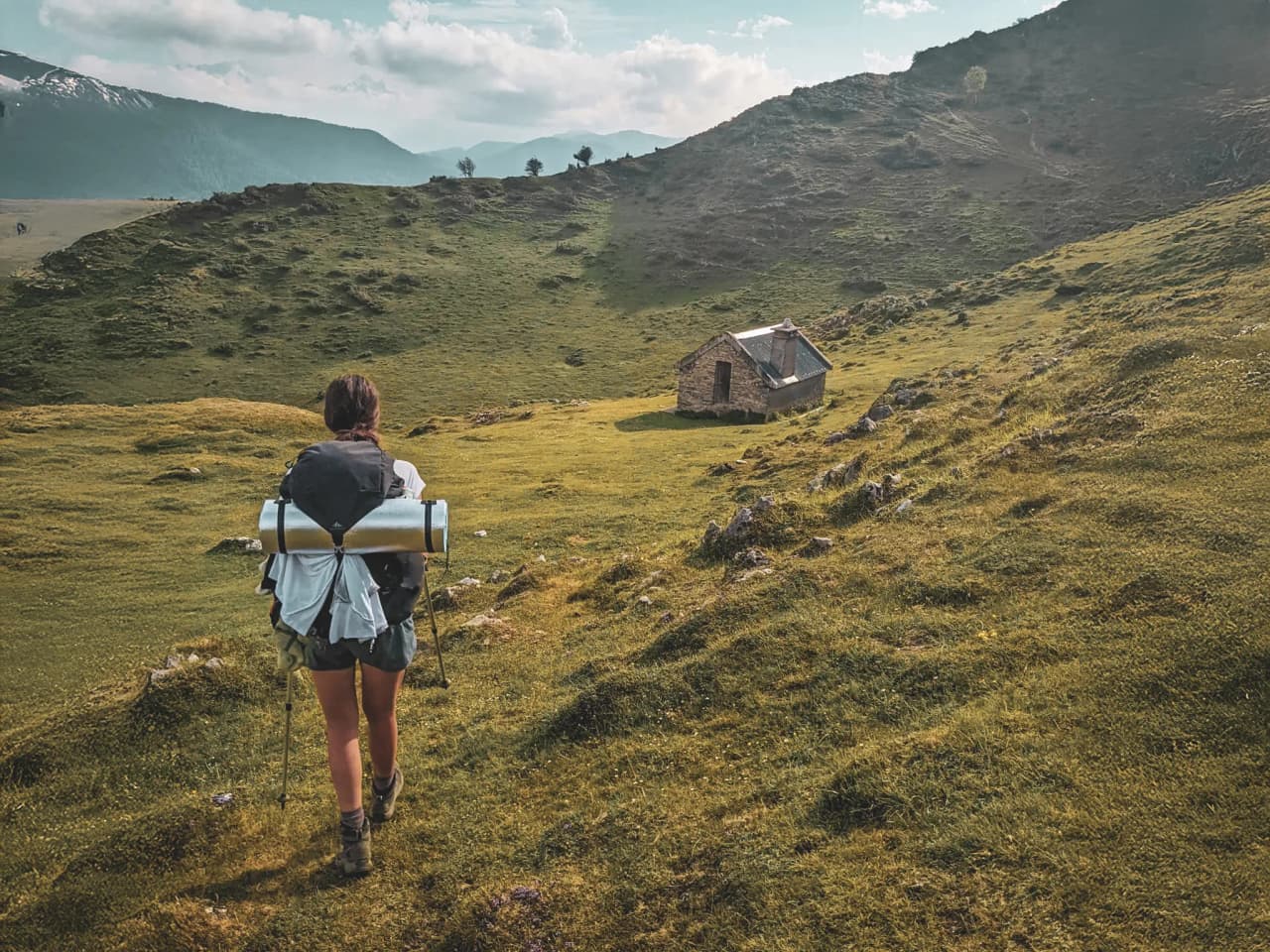 Randonneuse sur un chemin verdoyant, devant un chalet pittoresque dans les Pyrénées.