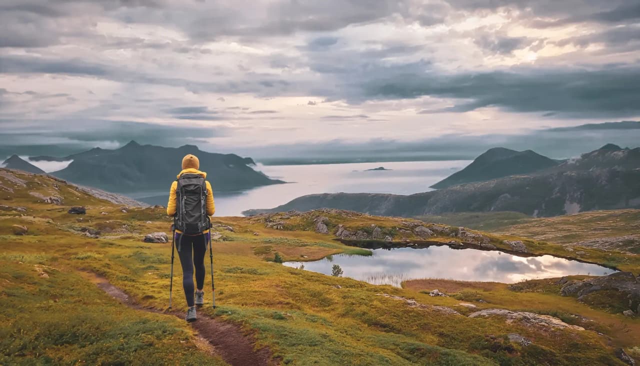 Femme en randonnée sur l'île de Senja, devant des fjords majestueux et des lacs glaciaires.