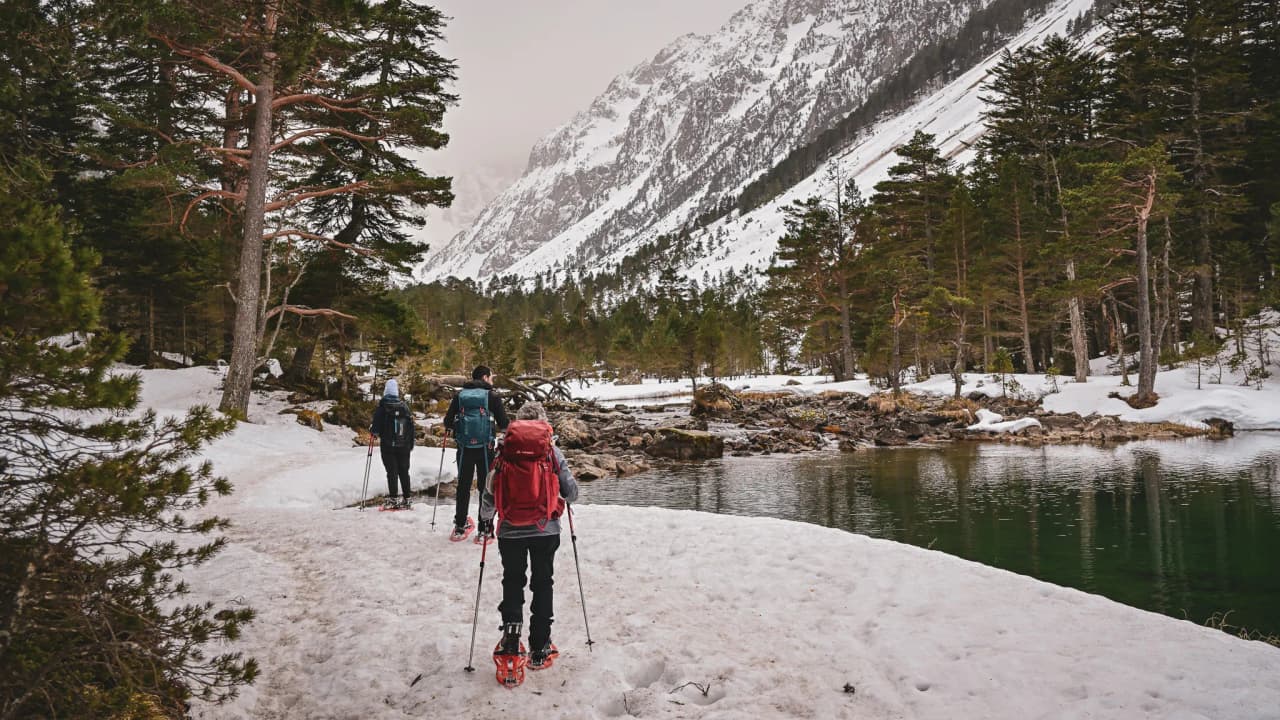 Group of hikers on snowshoes on a snowy path near a lake in the Pyrenees.