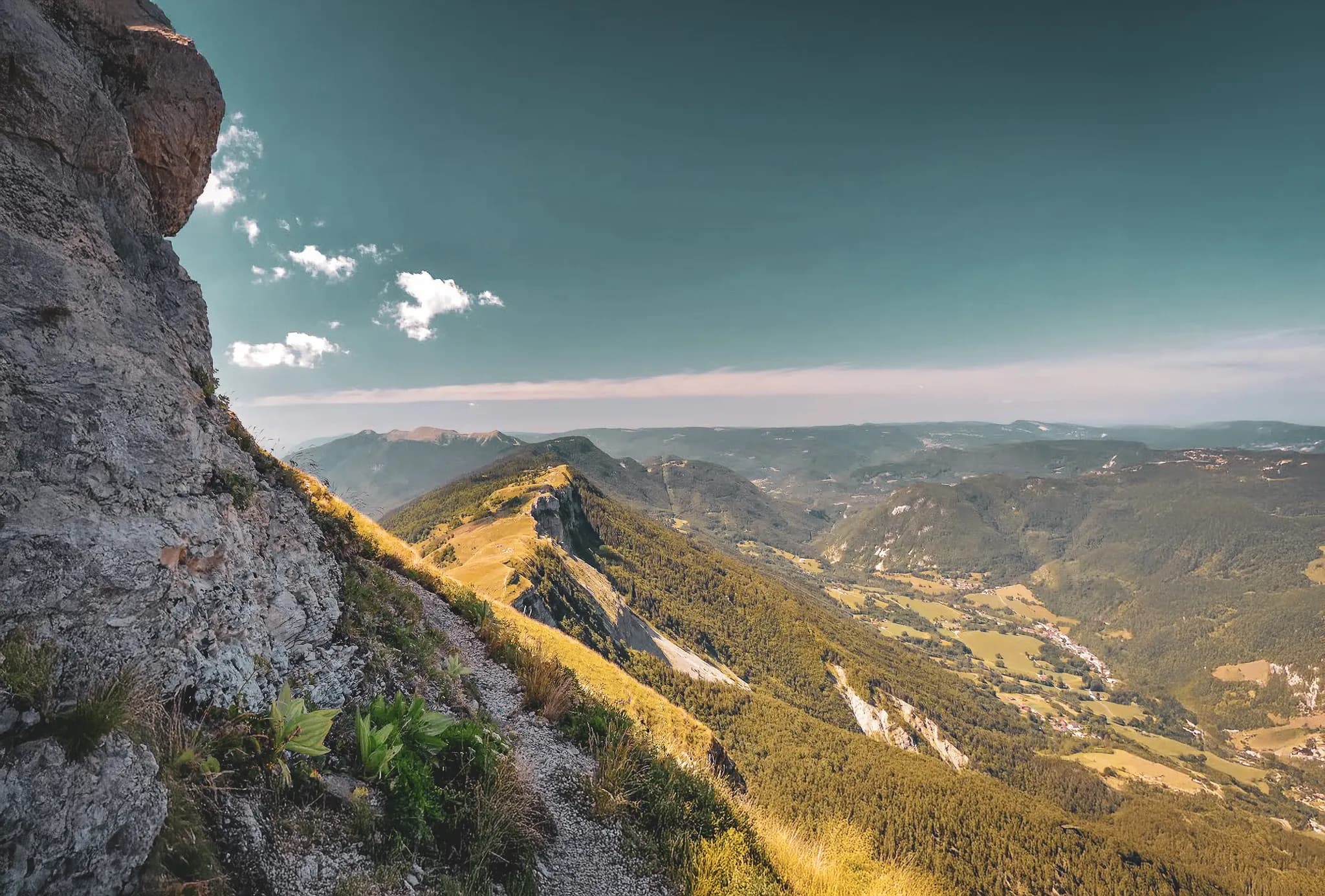 A panorama of majestic mountains, with snow-capped peaks and rolling landscapes below. The scene captures craggy cliffs mingling with verdant vegetation, while a sky
