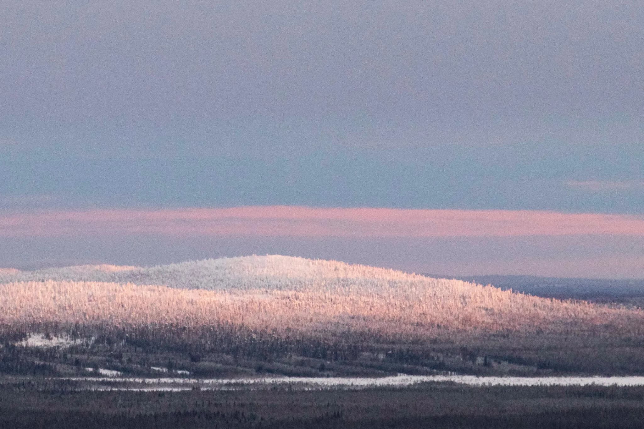Vue panoramique des collines enneigées de Laponie, baignées dans une lumière douce au crépuscule.