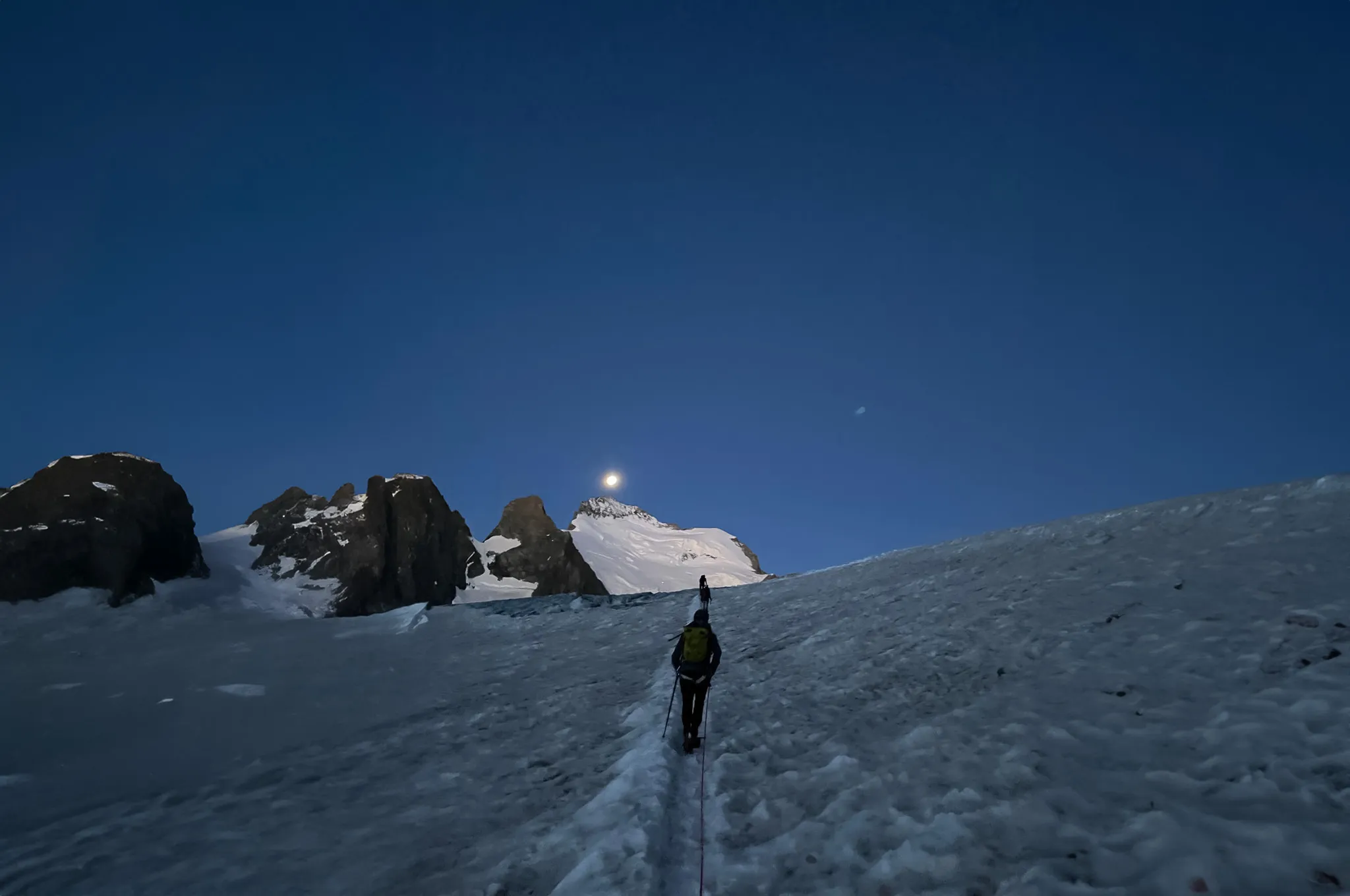 Un alpiniste gravissant un glacier sous la lumière de la lune dans les Écrins, ambiance magique.